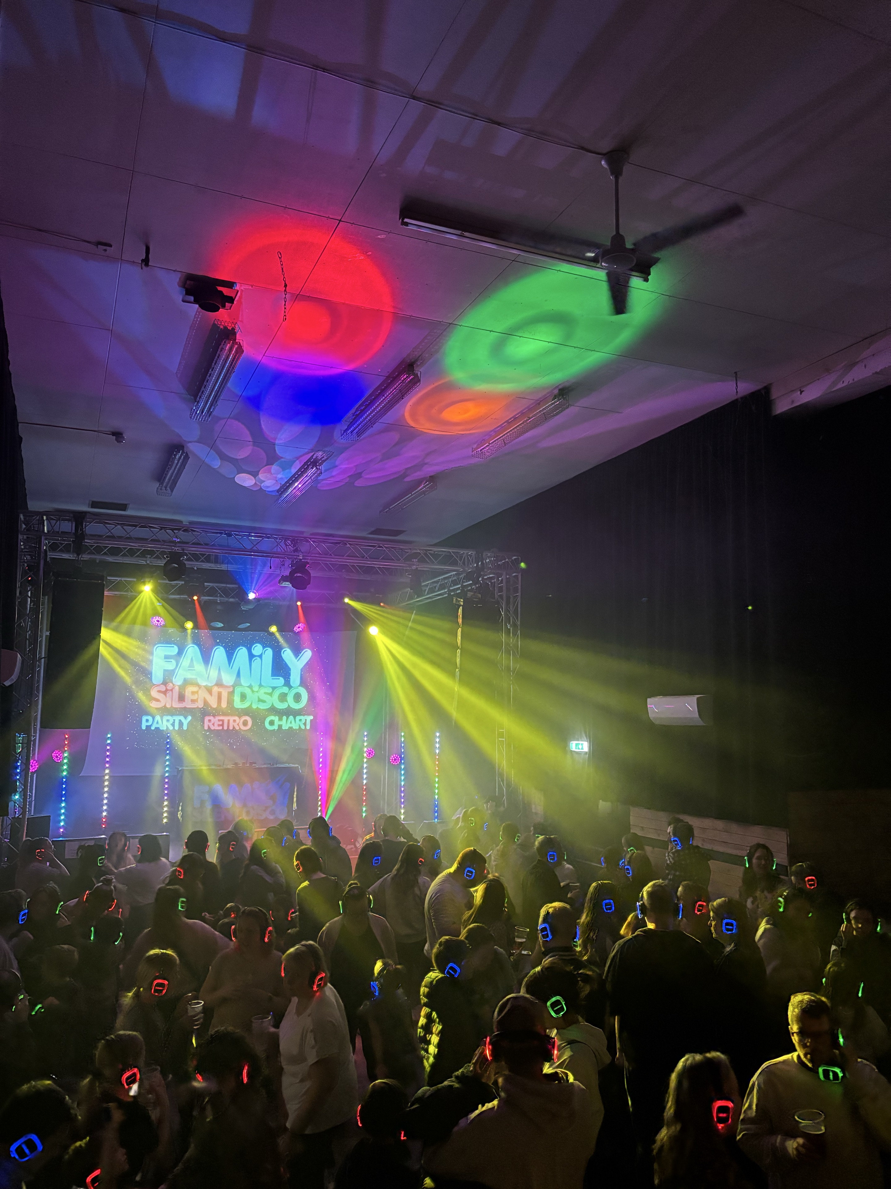 Families dancing in glowing headphones beneath a Family Silent Disco screen