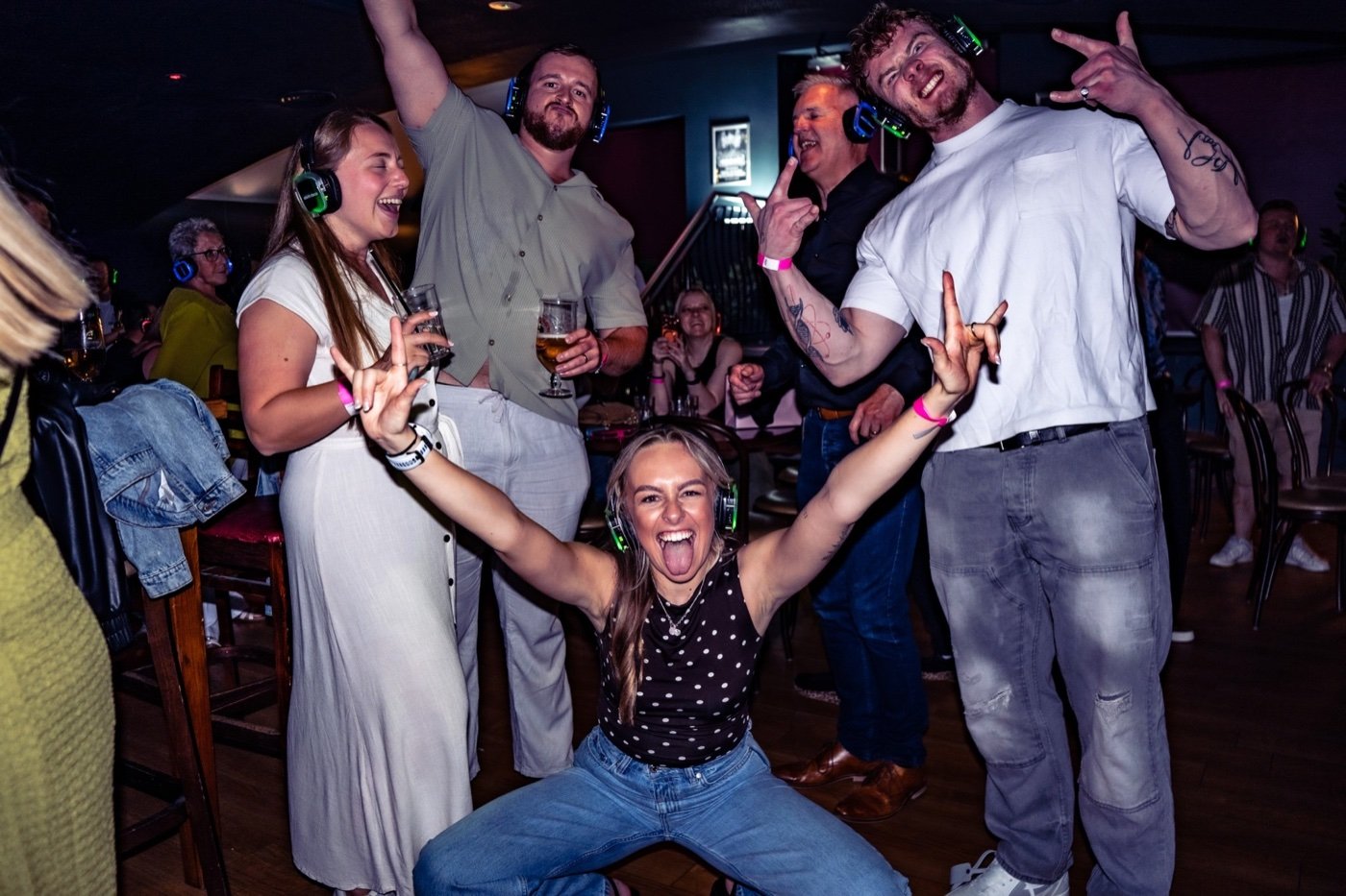 A group of friends dancing with arms raised in light-up headphones